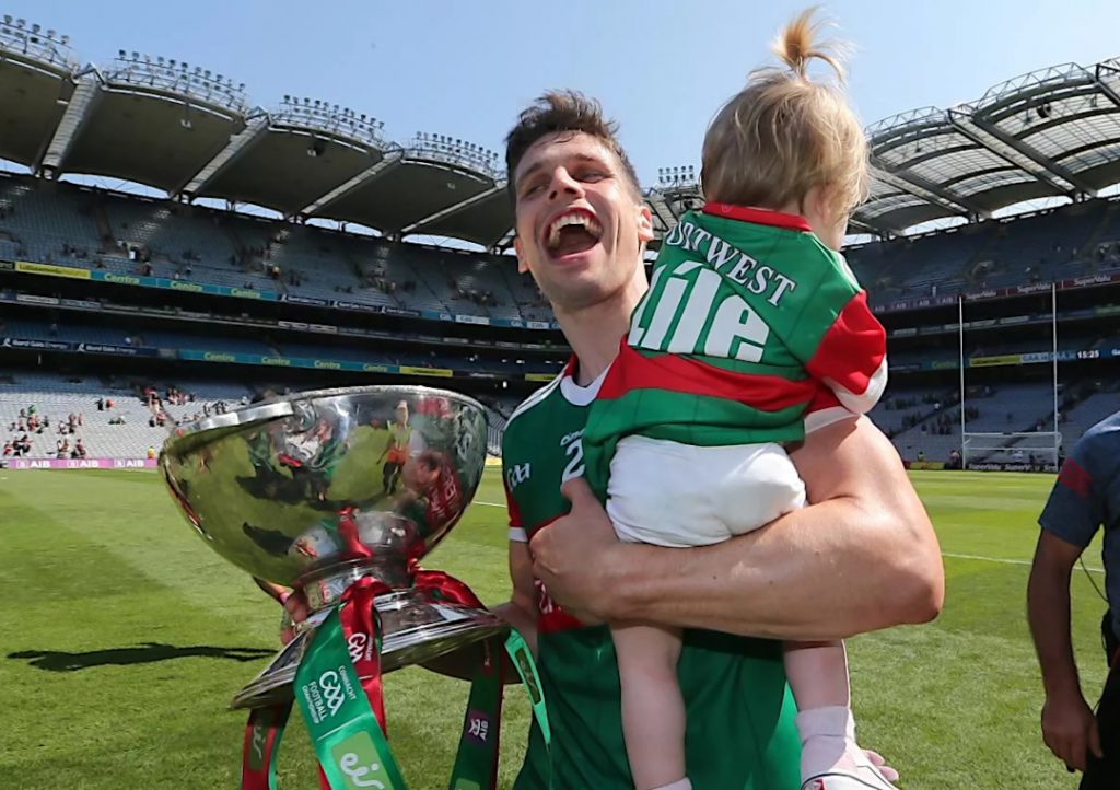 Lee Keegan holding his child in one hand and a trophy in the other