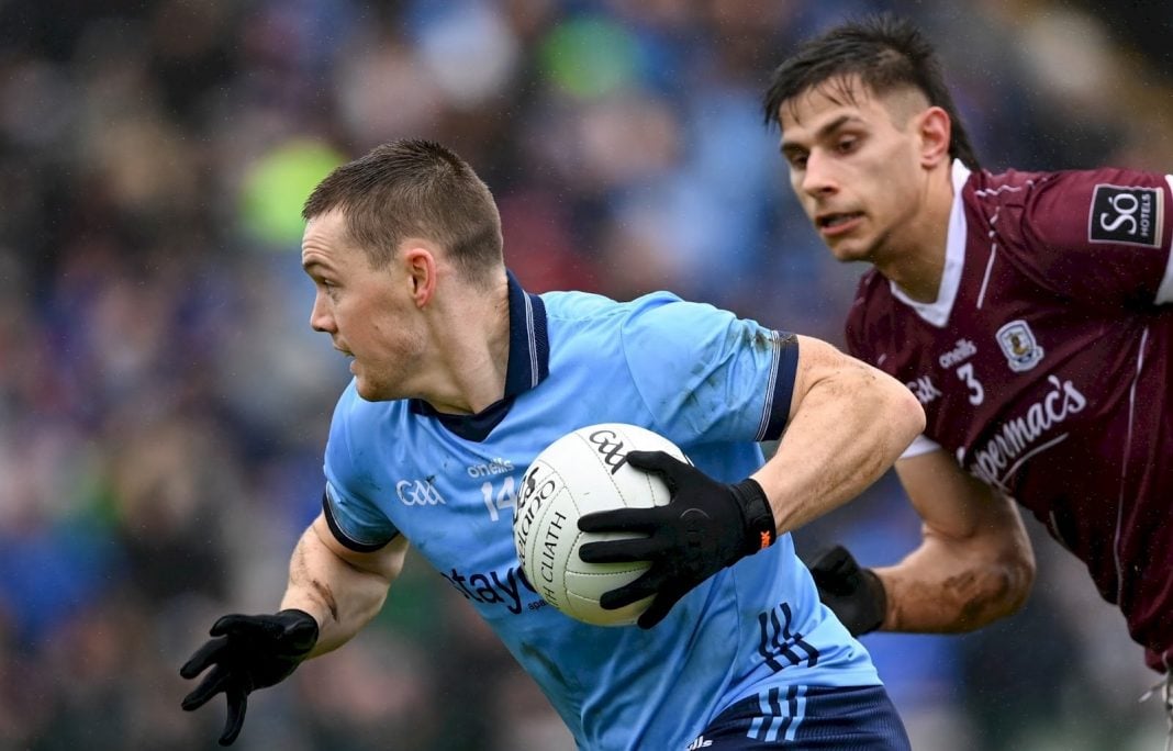 Galway footballer closes in on a Dublin GAA player holding the ball